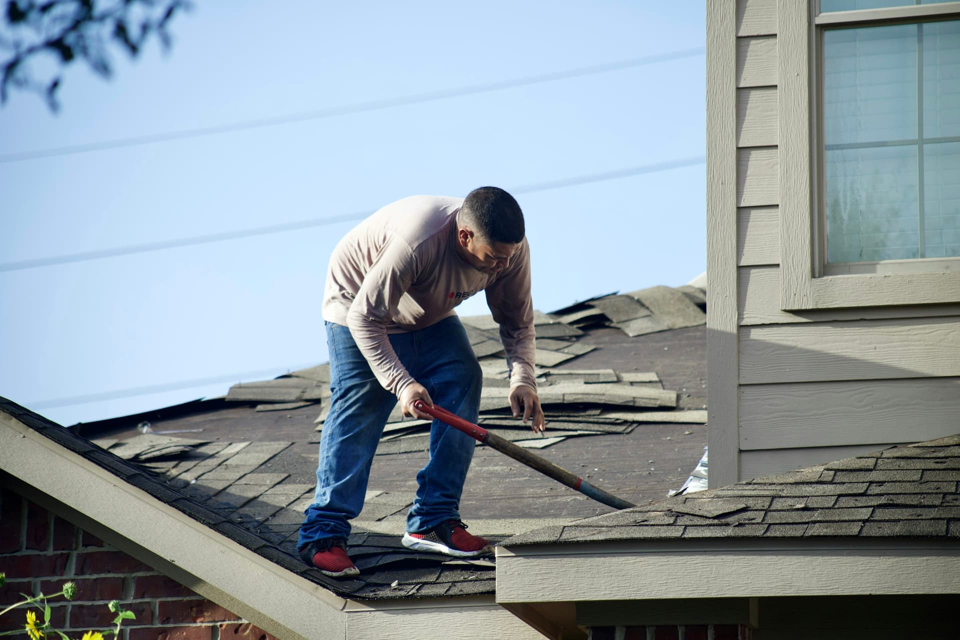 Roofer tearing off old shingles before a roof replacement