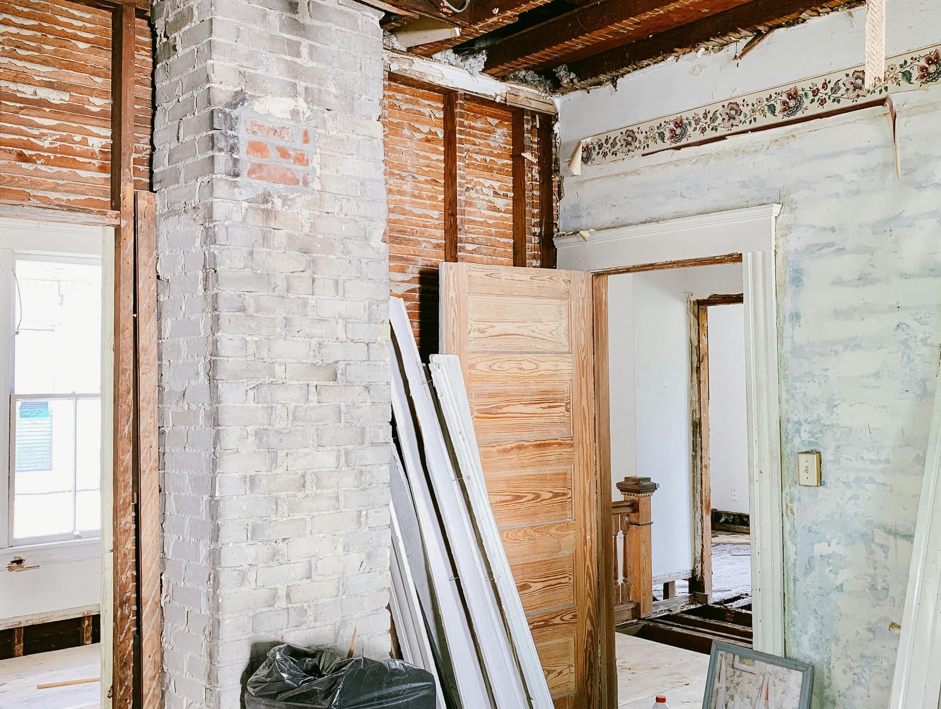 Interior of a home mid-rebuild showing exposed ceiling joists, brick chimney, and new materials staged for reconstruction