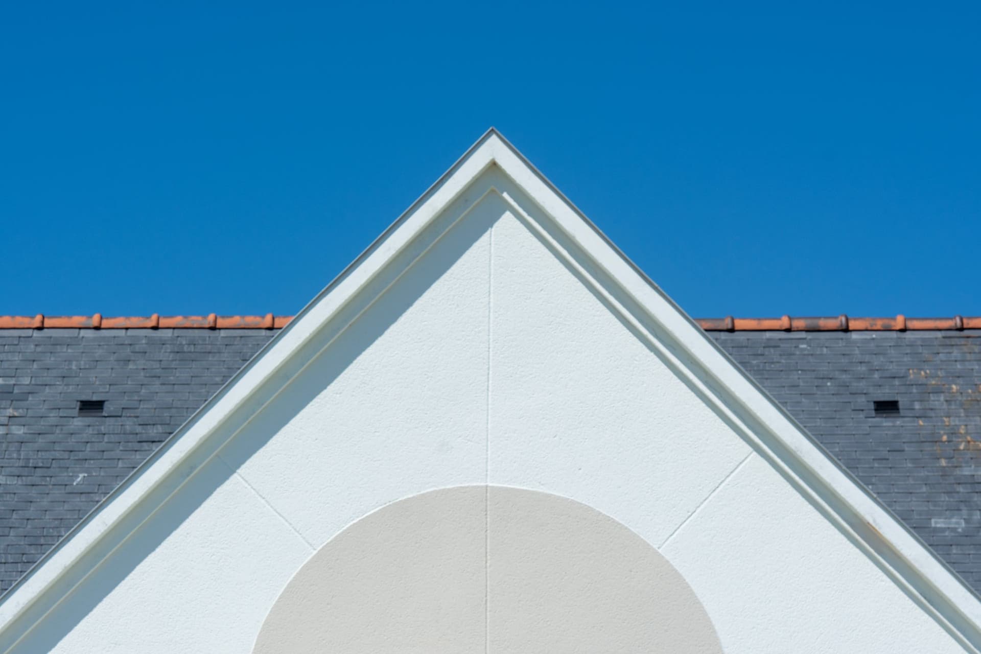 Gable end of a house showing the slope of the roof against a blue sky