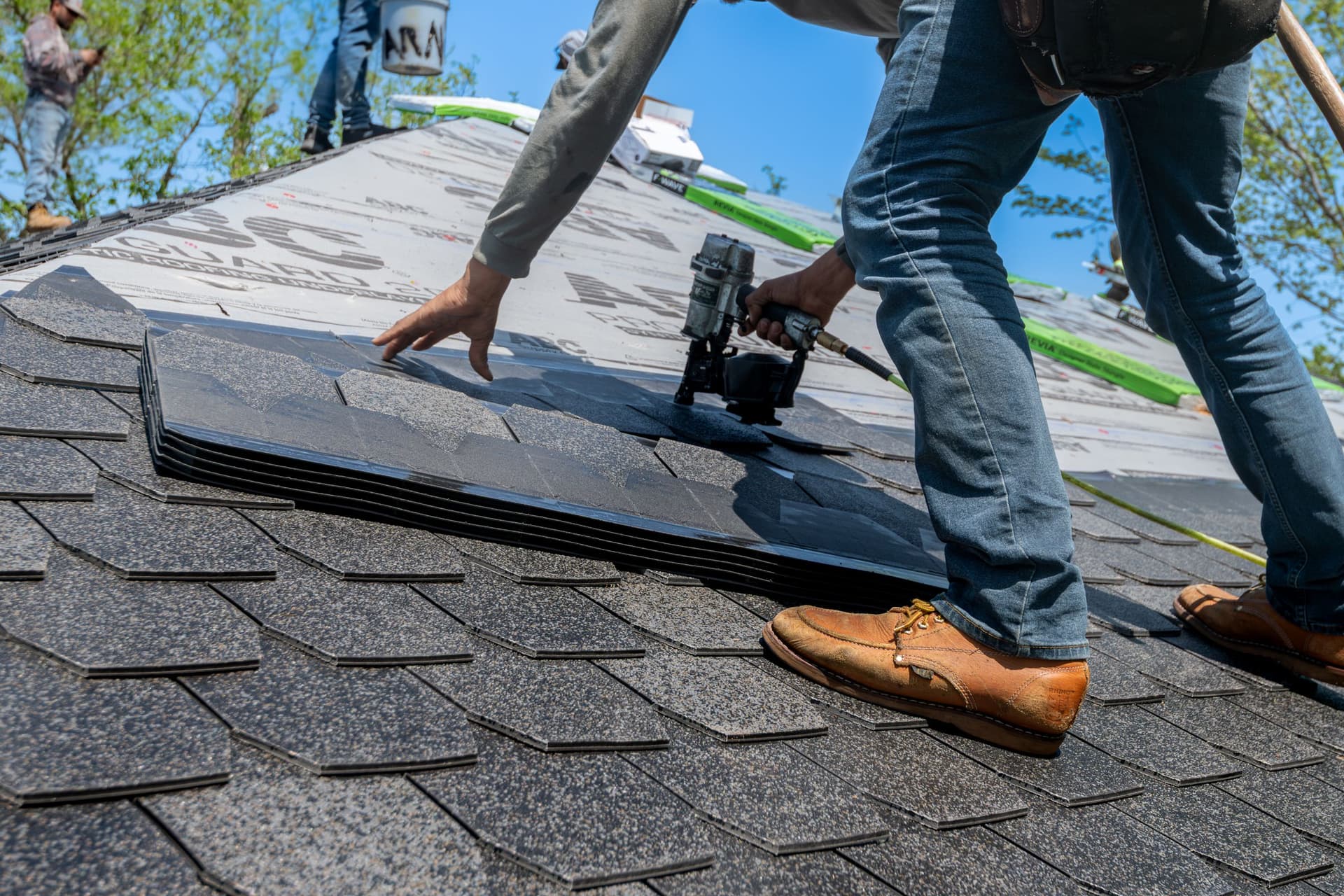 Roofer nailing architectural shingles with a nail gun